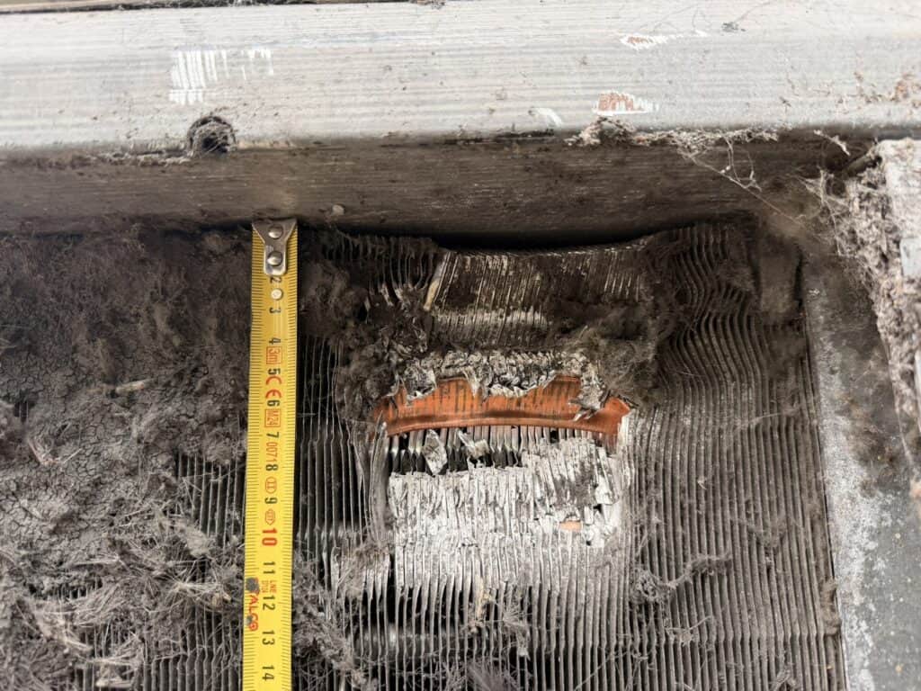 Uszkodzony element chłodniczy w instalacji HVAC, widoczny w wykopie z narzędziem pomiarowym.