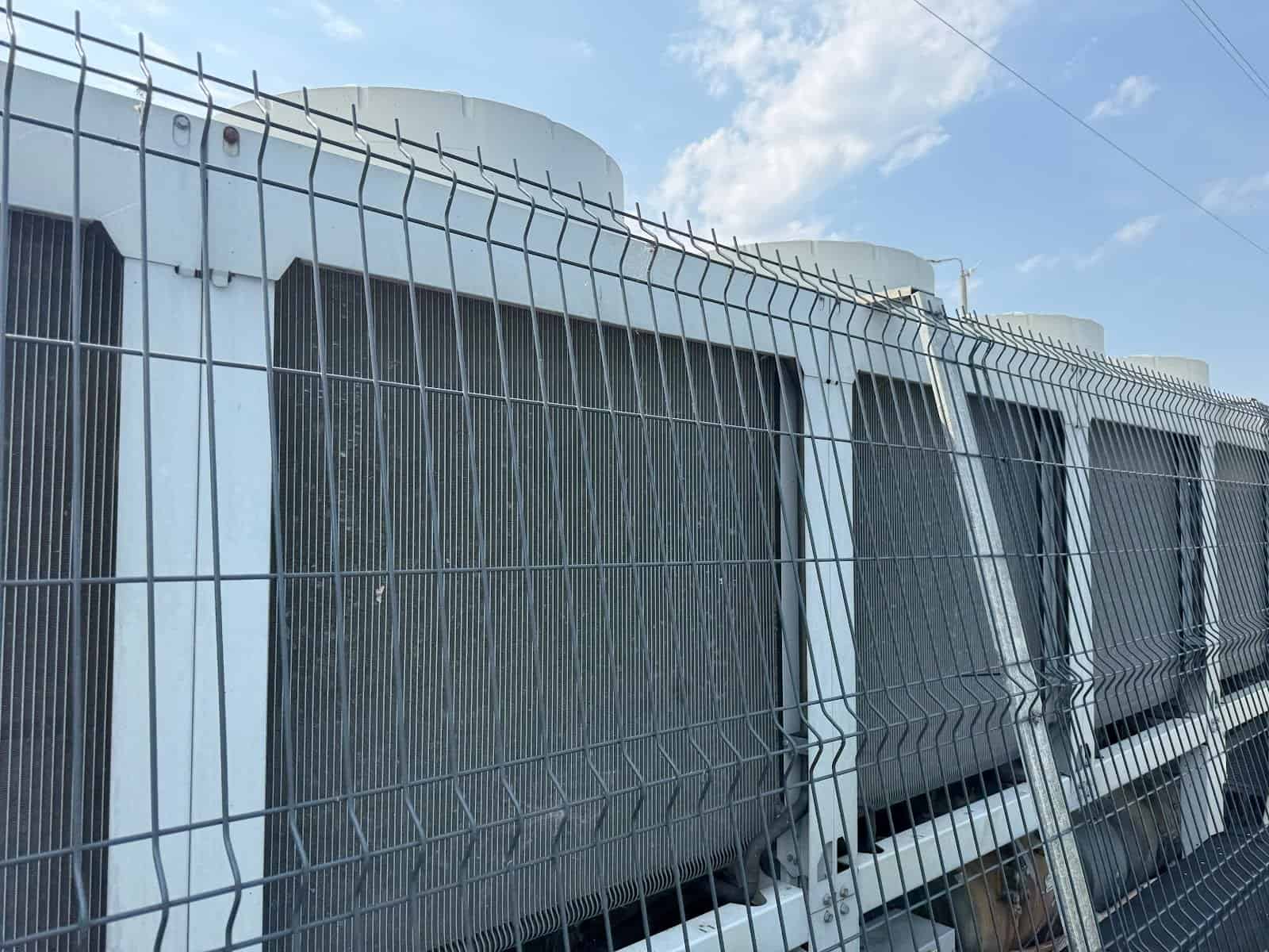 Skraplacze urządzeń chłodniczych na dachu hali za ogrodzeniem