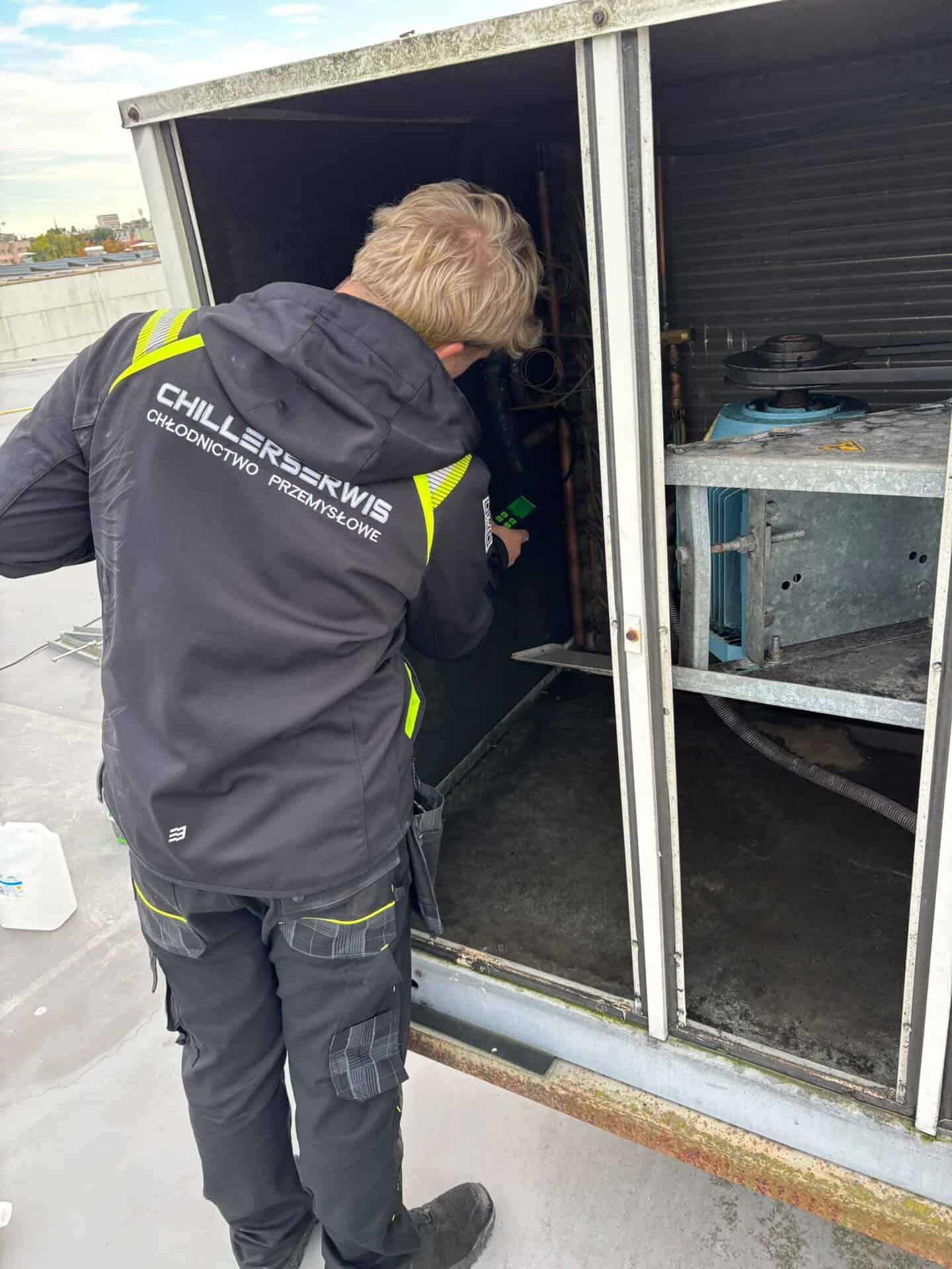 Technik ChillerSerwis przy otwartej sekcji rooftopa podczas mycia skraplacza